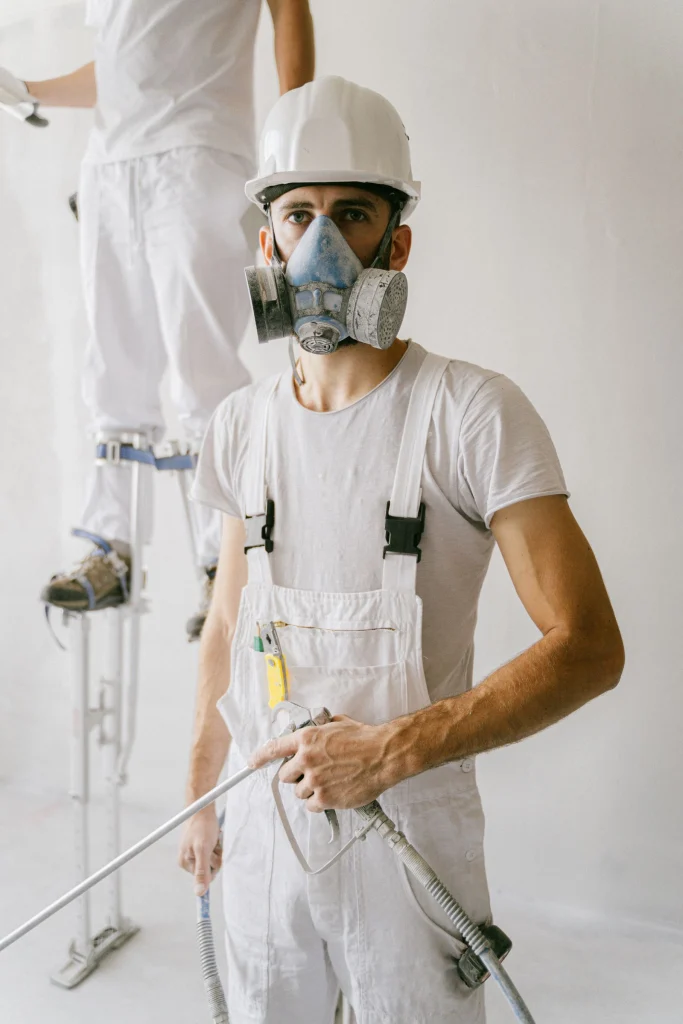 Trabajador con casco y máscara de protección respiratoria mirando a cámara en un entorno industrial